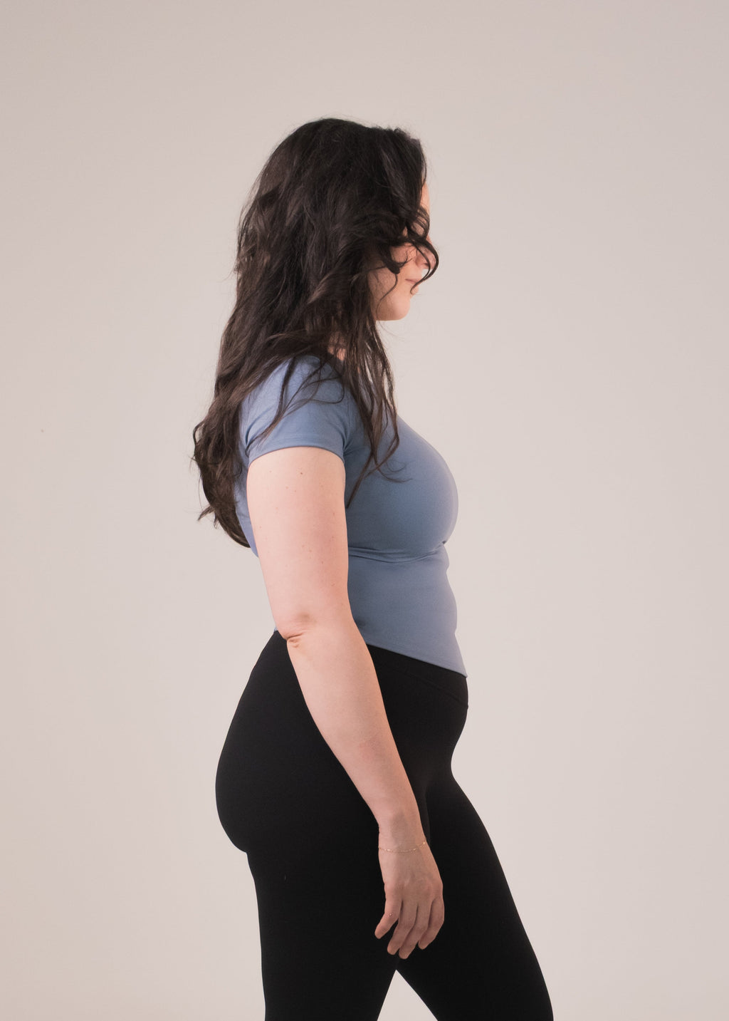 Woman wearing a blue shirt and black leggings standing against a plain background