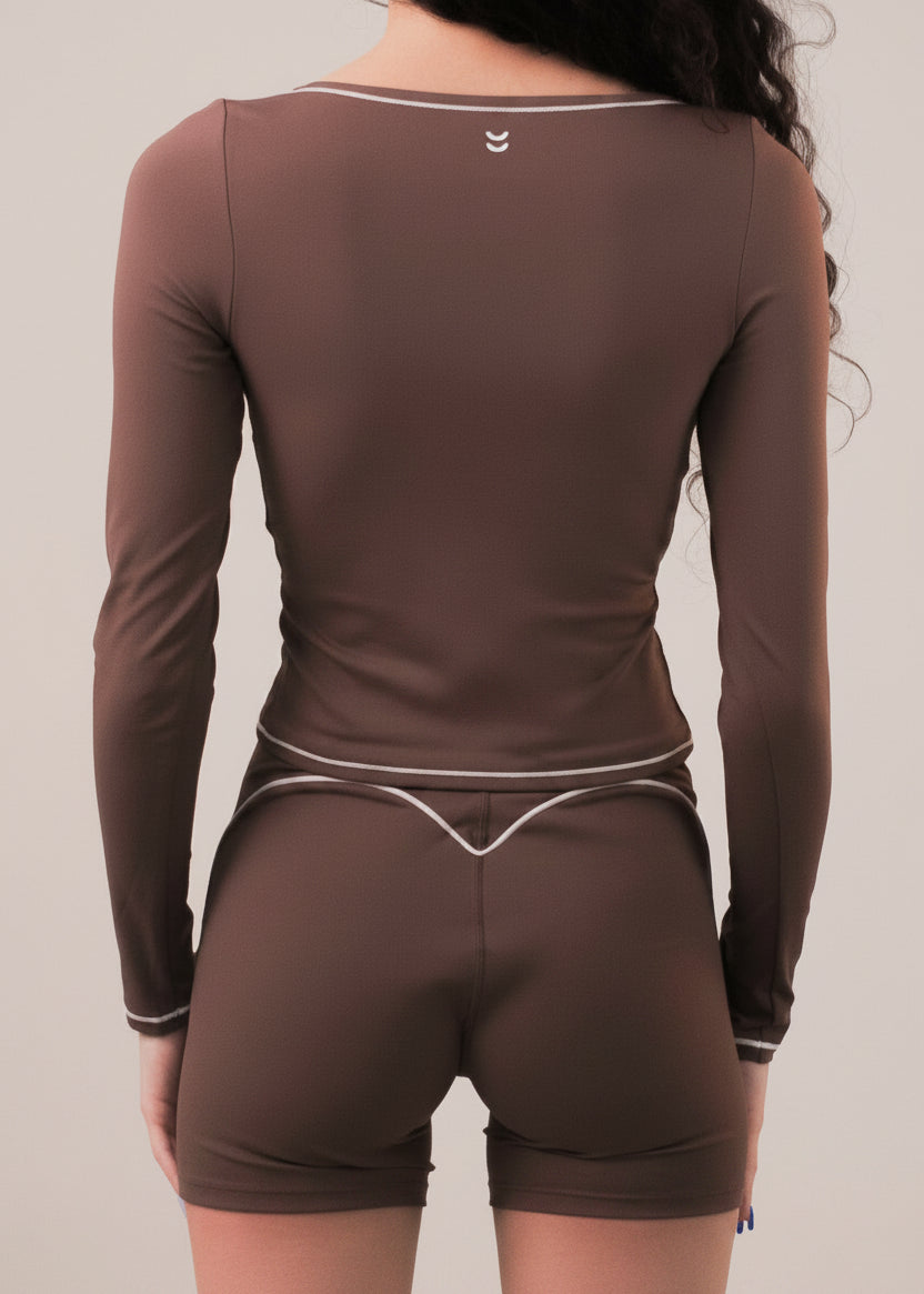 Person wearing a brown long-sleeve top and shorts on a beige background