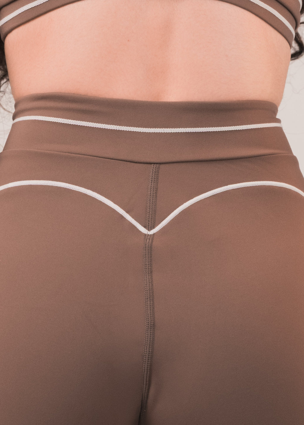 Person wearing brown athletic shorts and crop top on a plain background