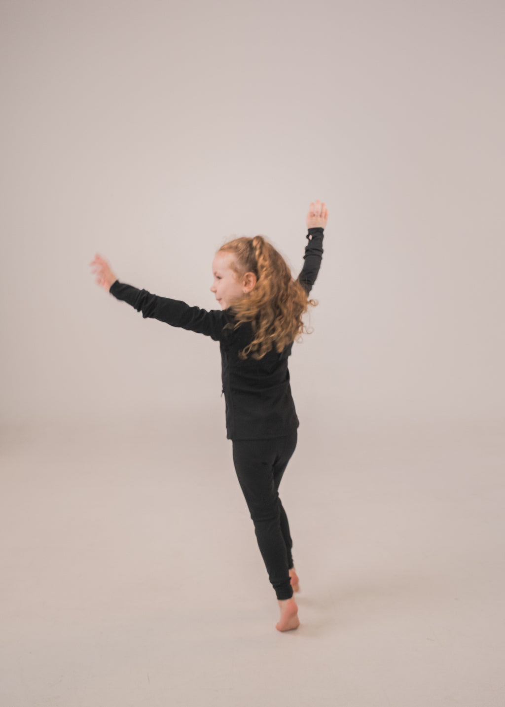 Child in a black outfit standing with arms outstretched on a plain background