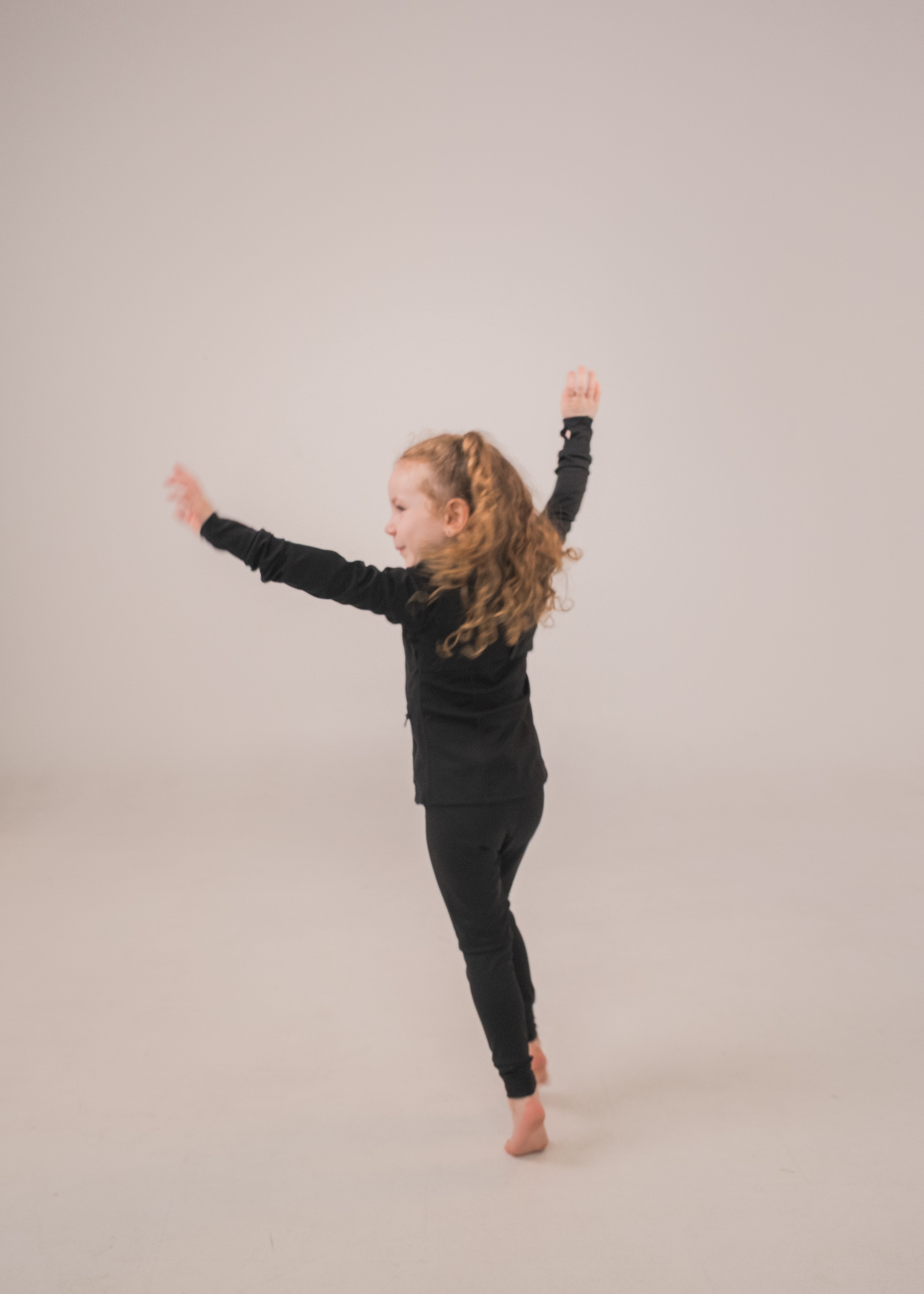 Child in a black outfit standing with arms outstretched on a plain background