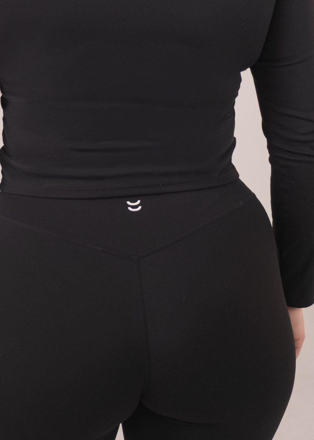 Person wearing a black long-sleeve top and pants on a beige background