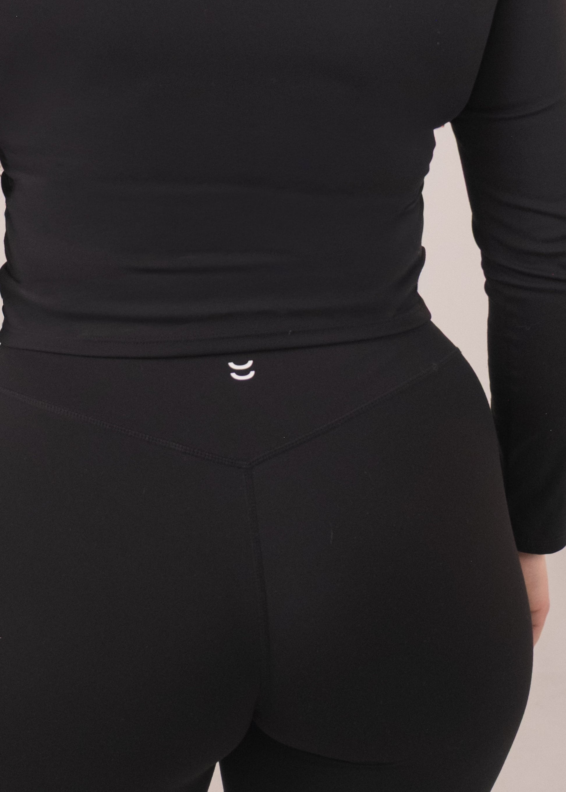 Person wearing a black long-sleeve top and pants on a beige background