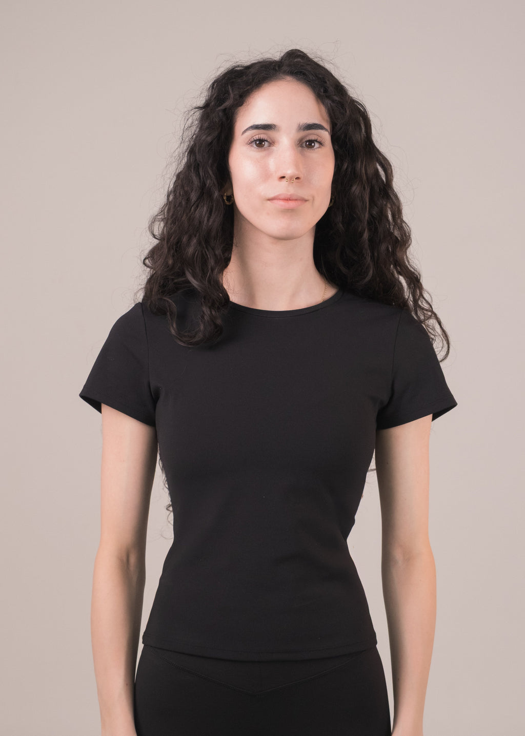 Woman wearing a black t-shirt and black pants against a beige background