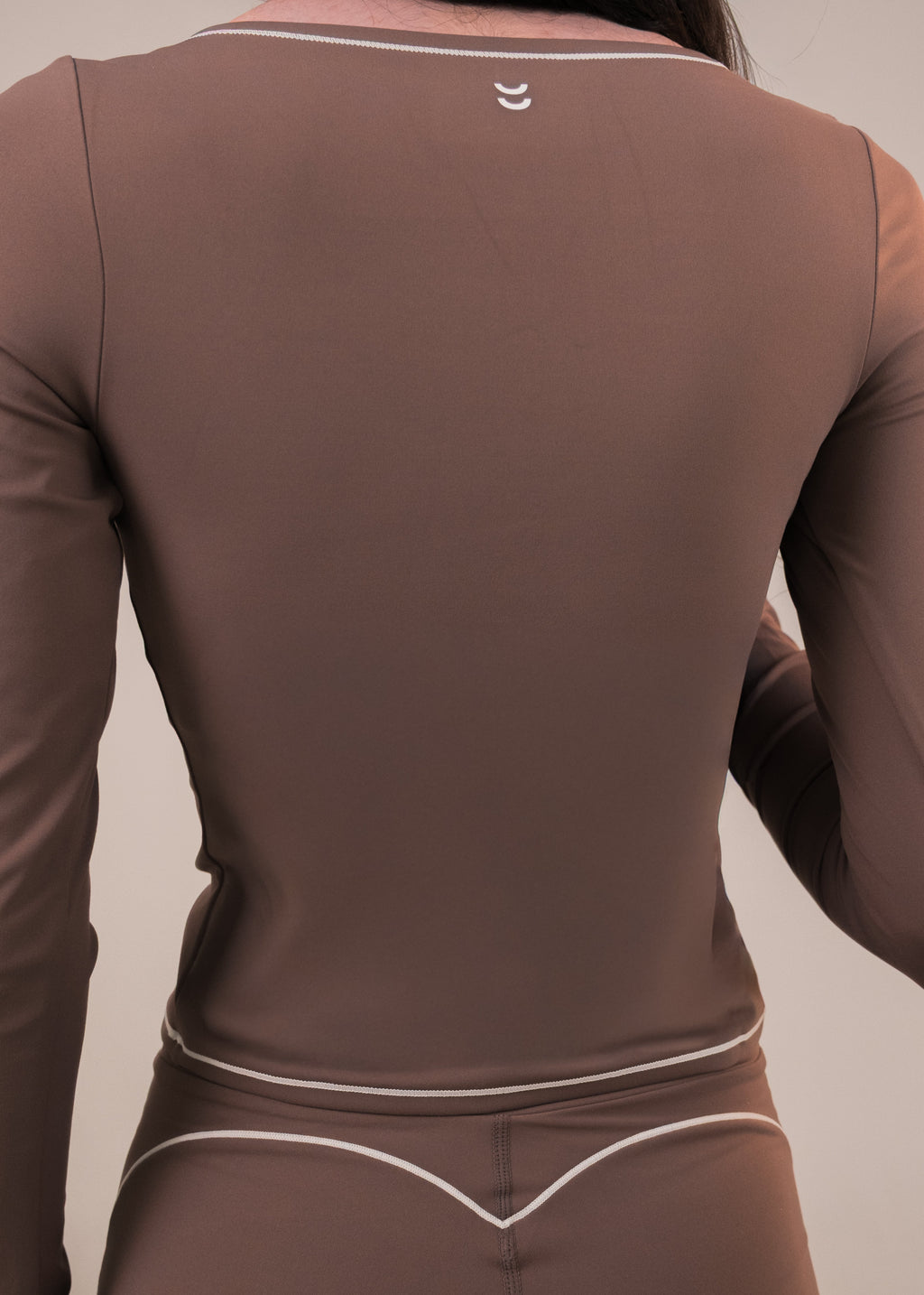 Brown long-sleeve athletic top with a logo on the back against a neutral background