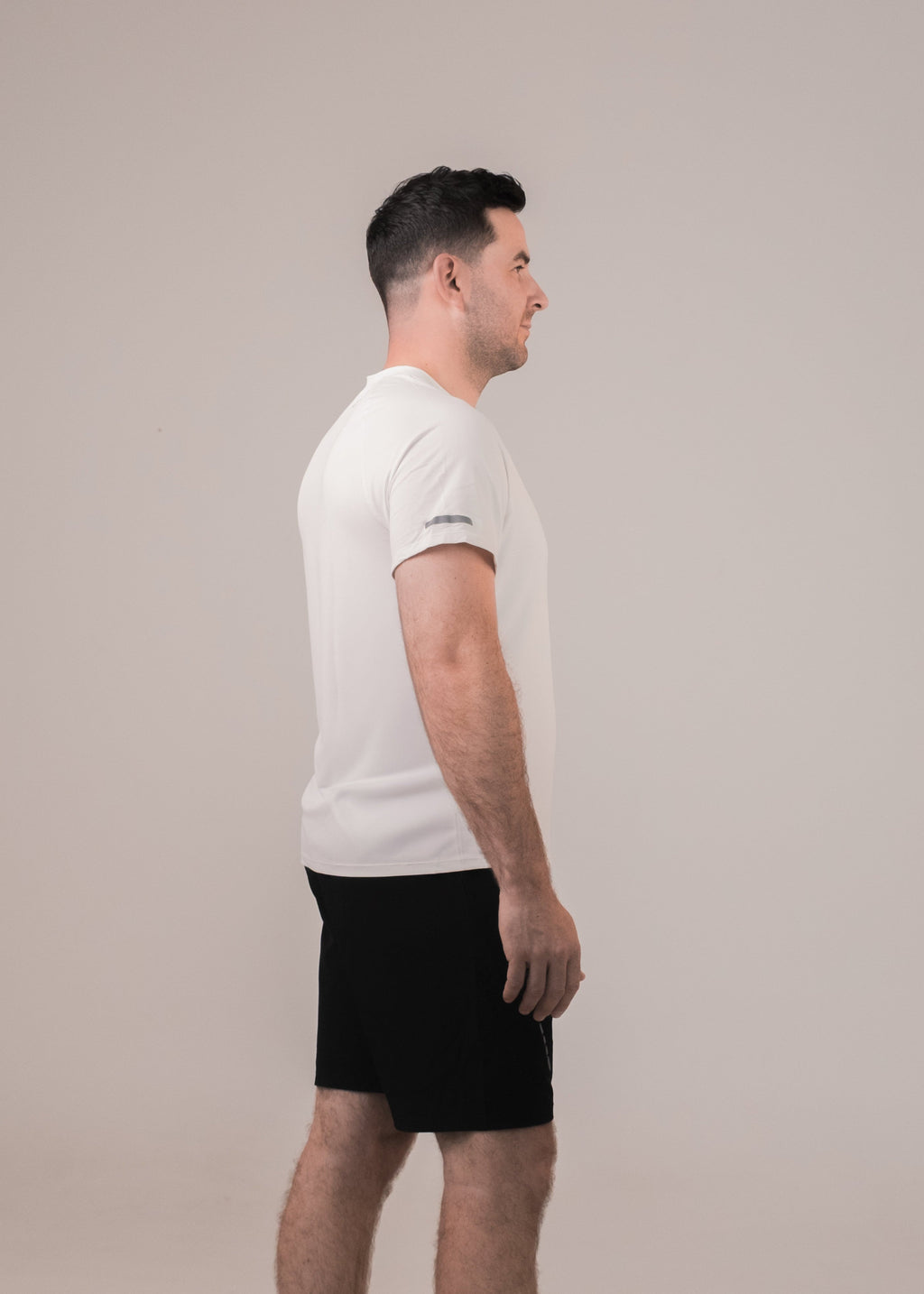 Man wearing a white t-shirt and black shorts standing against a plain background