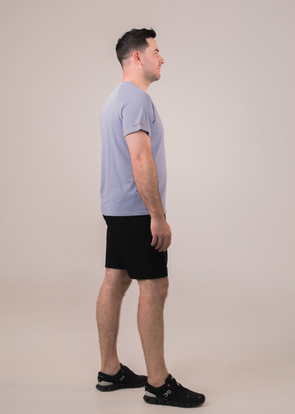 Man wearing a light blue shirt and black shorts on a beige background