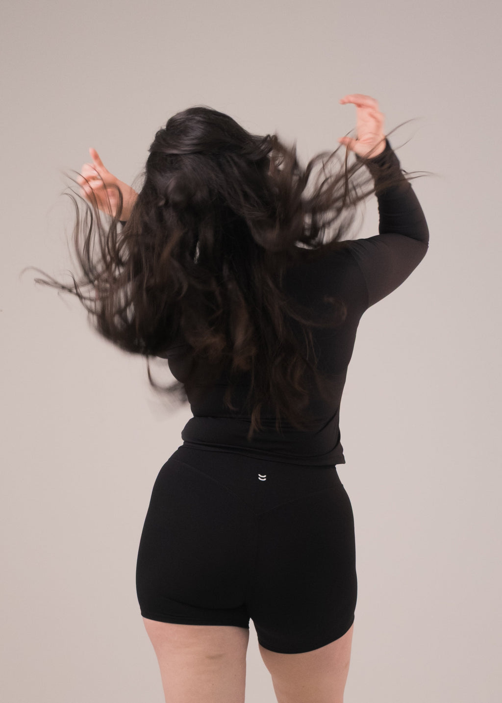 Person wearing a black outfit with flowing hair on a plain background
