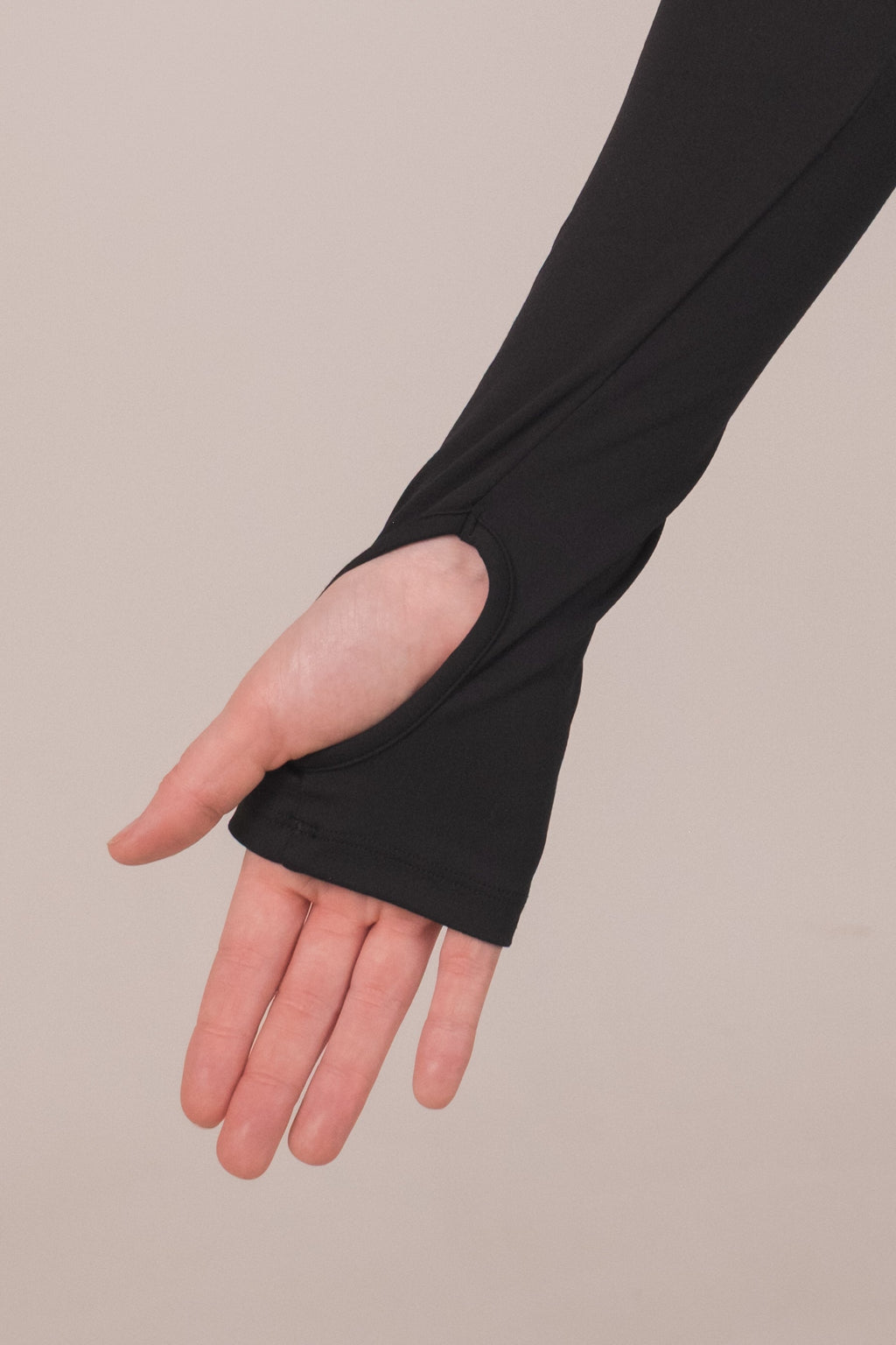 Person wearing a black long-sleeve top and black fingerless gloves on a beige background