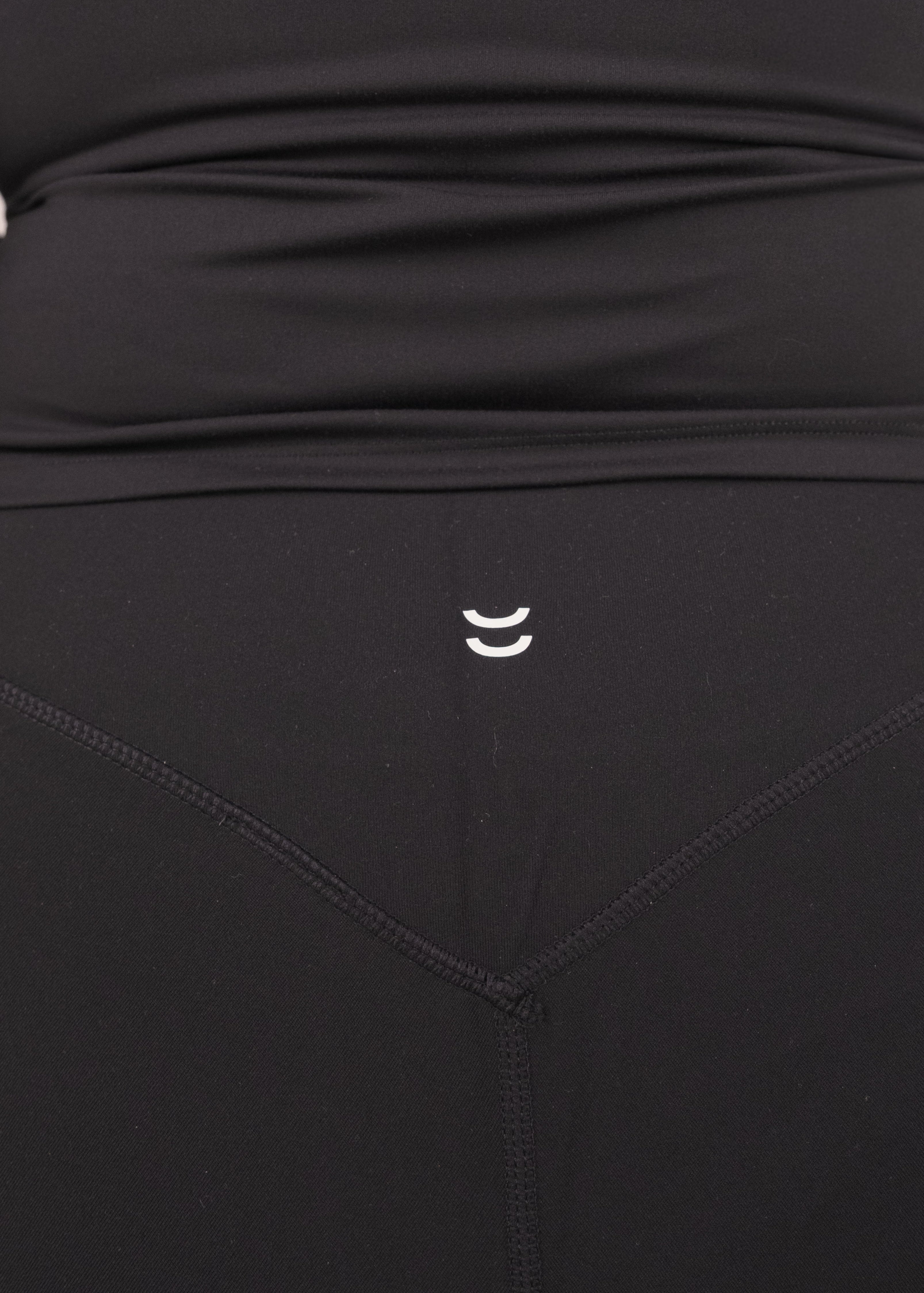 Black athletic outfit with a small logo on the waistband against a neutral background