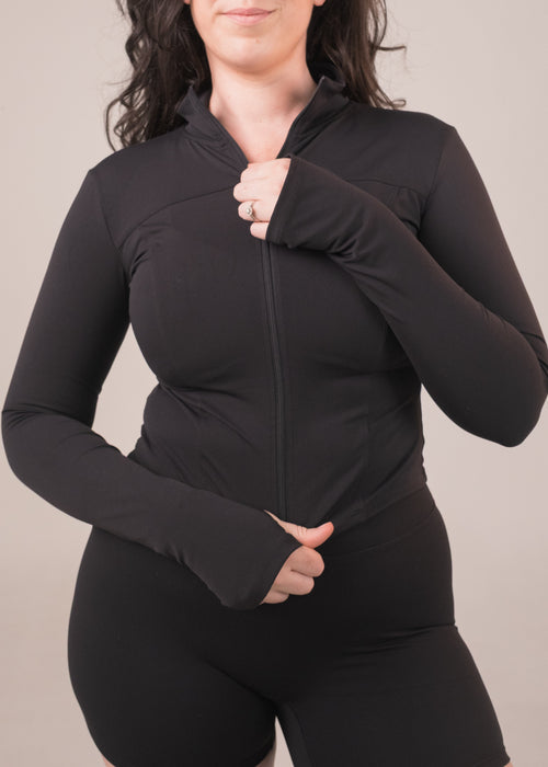 Woman wearing a black zip-up hoodie against a plain background