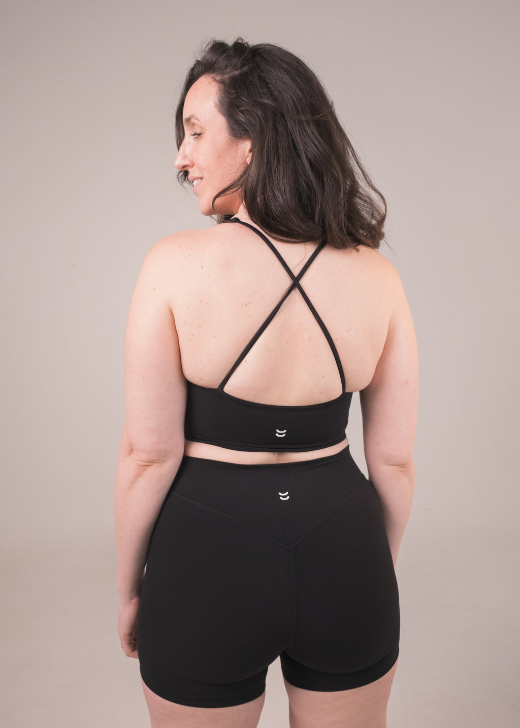 Woman wearing a black sports bra and shorts set against a plain background