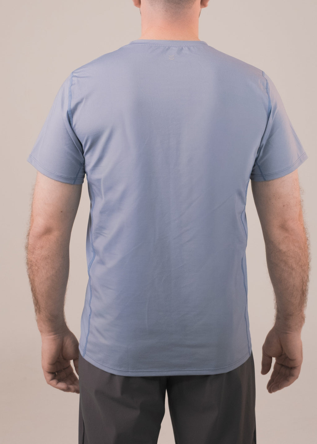 Man wearing a light blue t-shirt and dark pants against a beige background