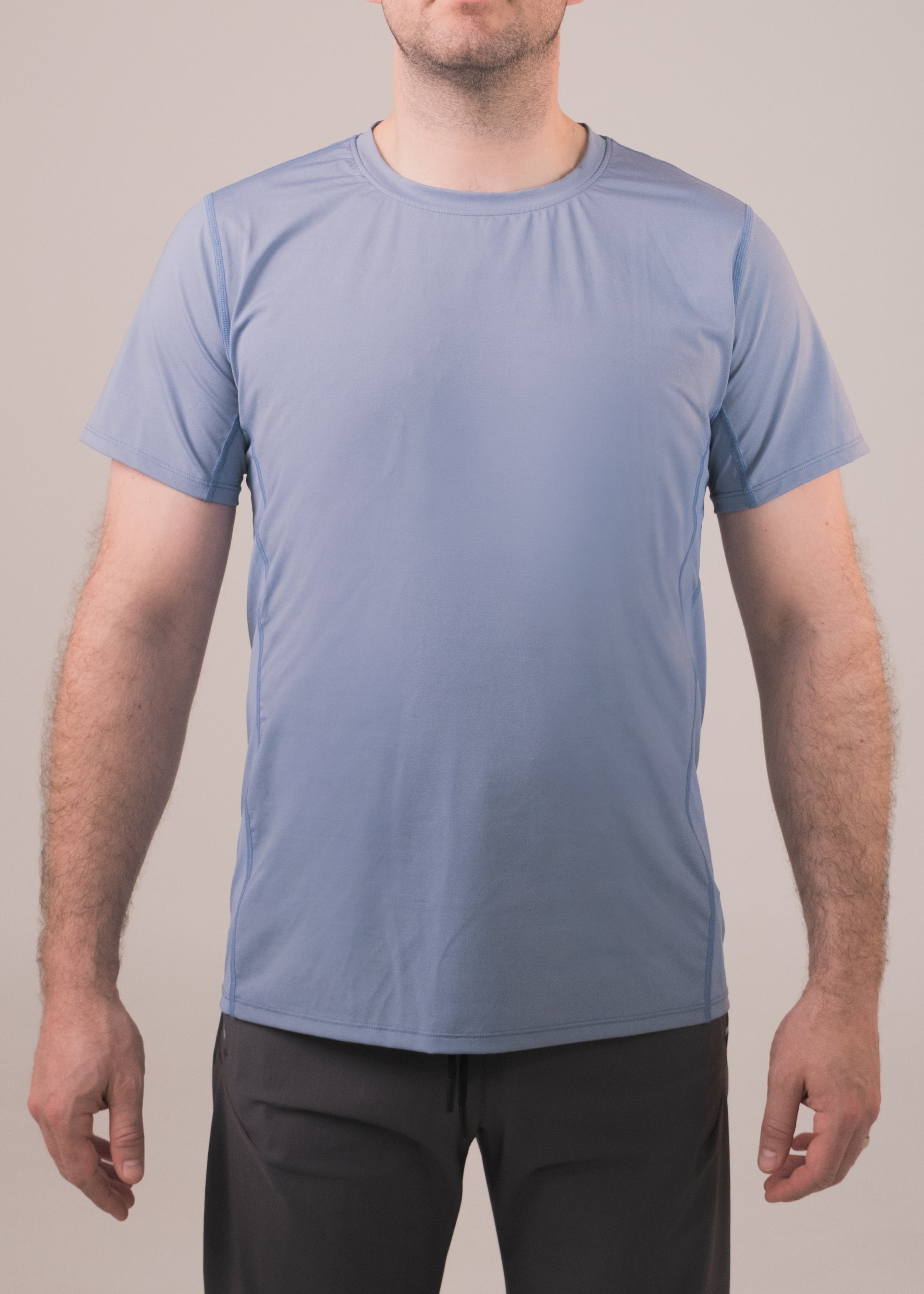 Man wearing a light blue t-shirt and black pants against a plain background