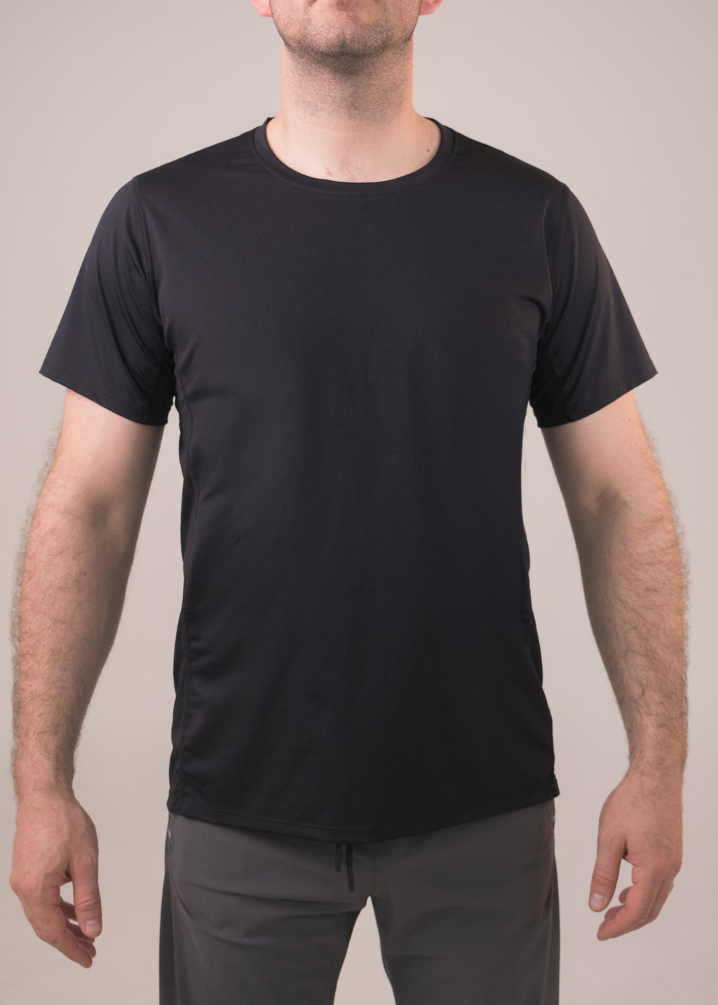 Man wearing a black t-shirt and gray pants against a plain background