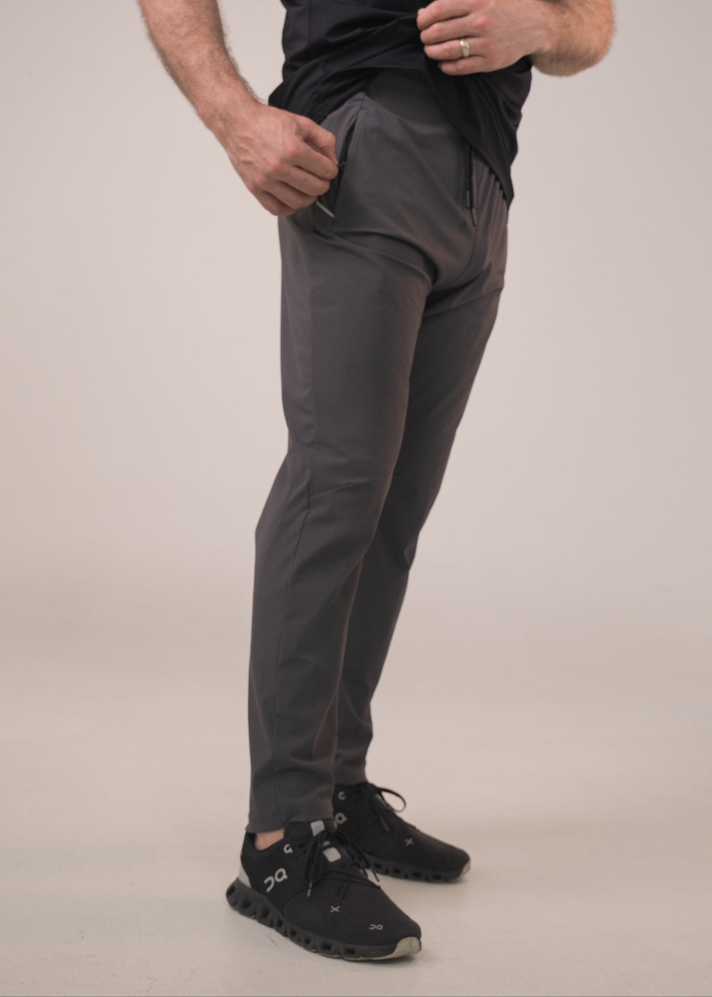 Person wearing dark gray pants and black shoes on a beige background