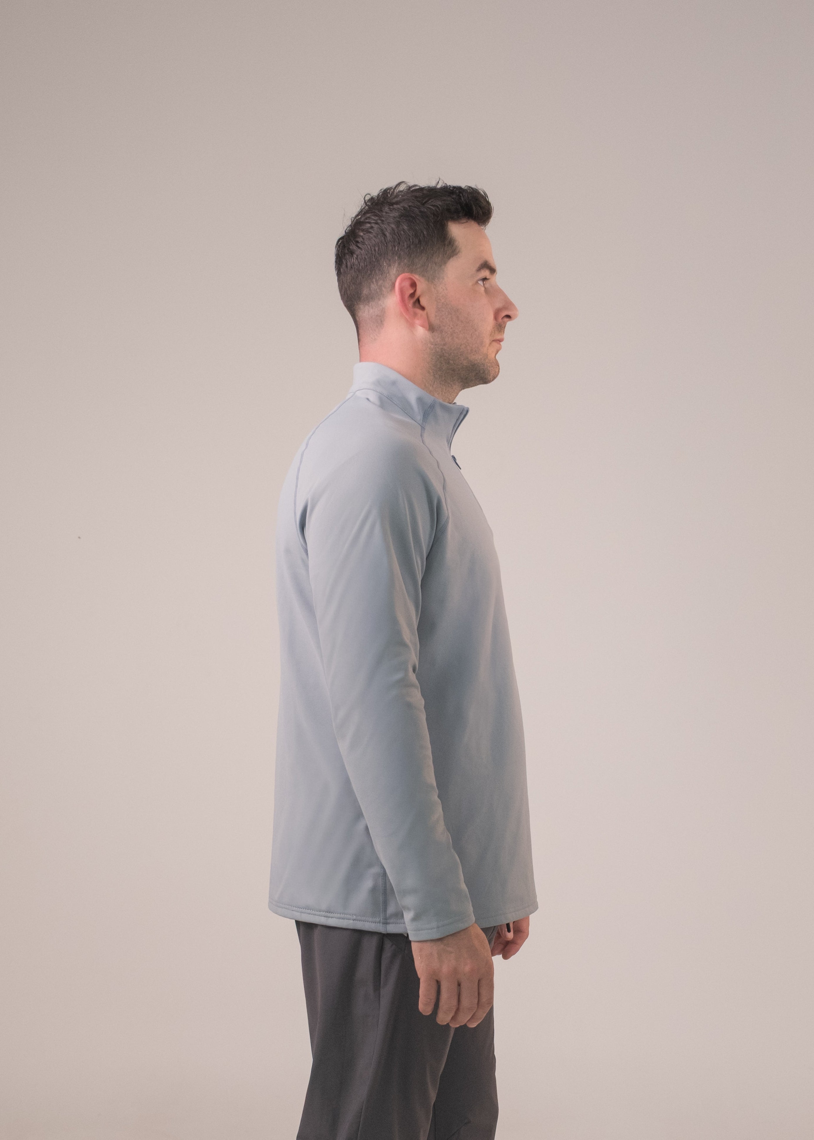 Man wearing a light gray sweater and dark pants on a beige background