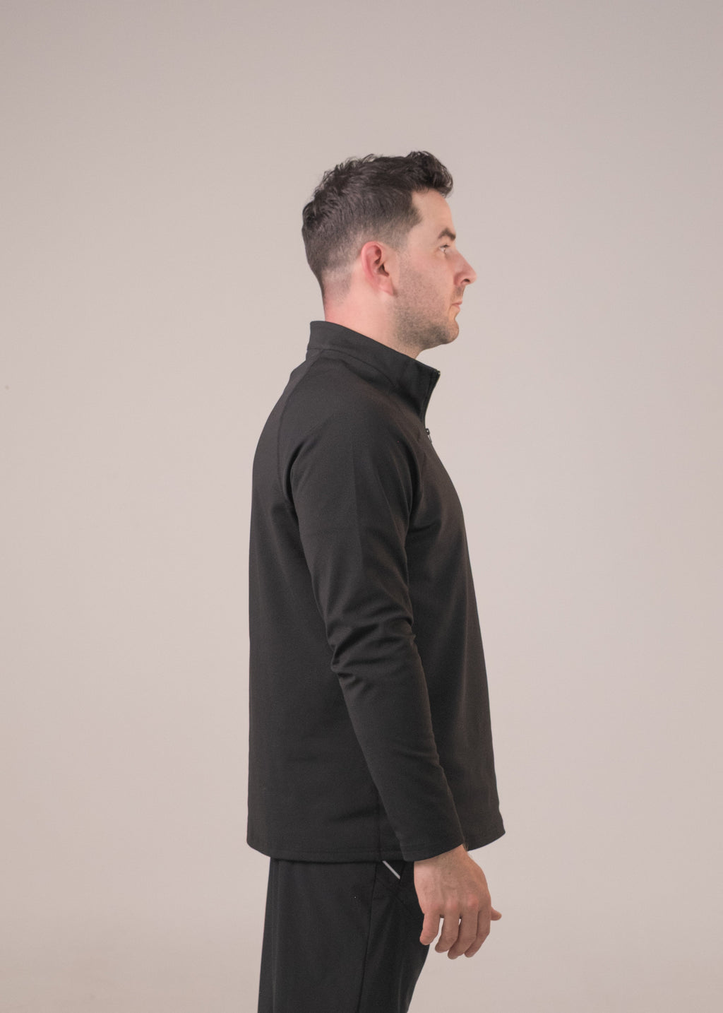 Man wearing a black outfit standing against a beige background