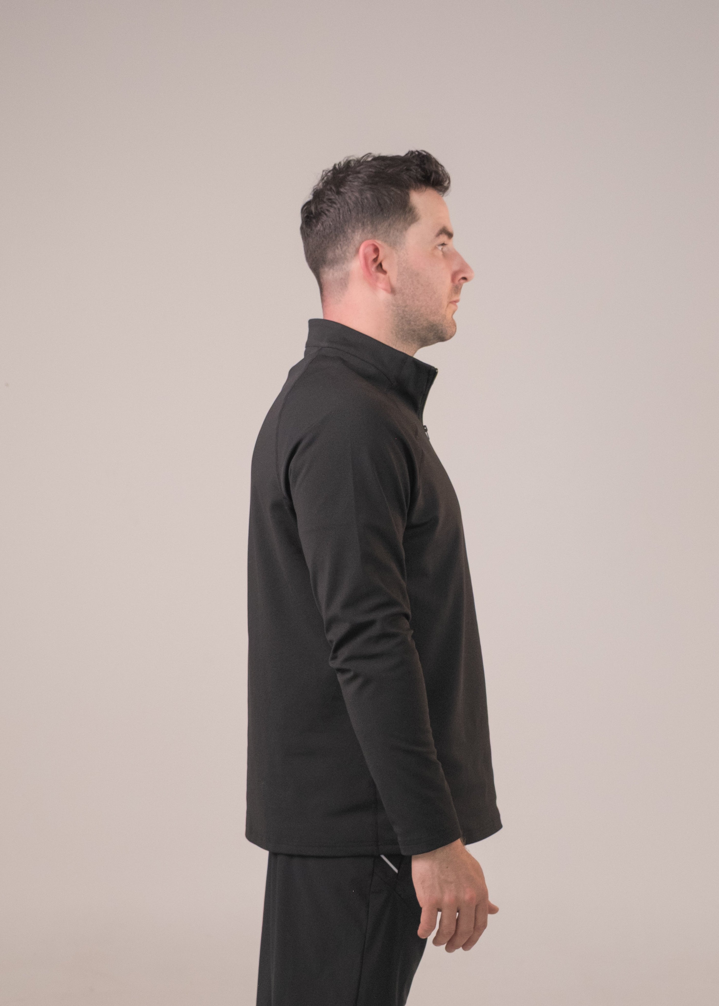 Man wearing a black outfit standing against a beige background