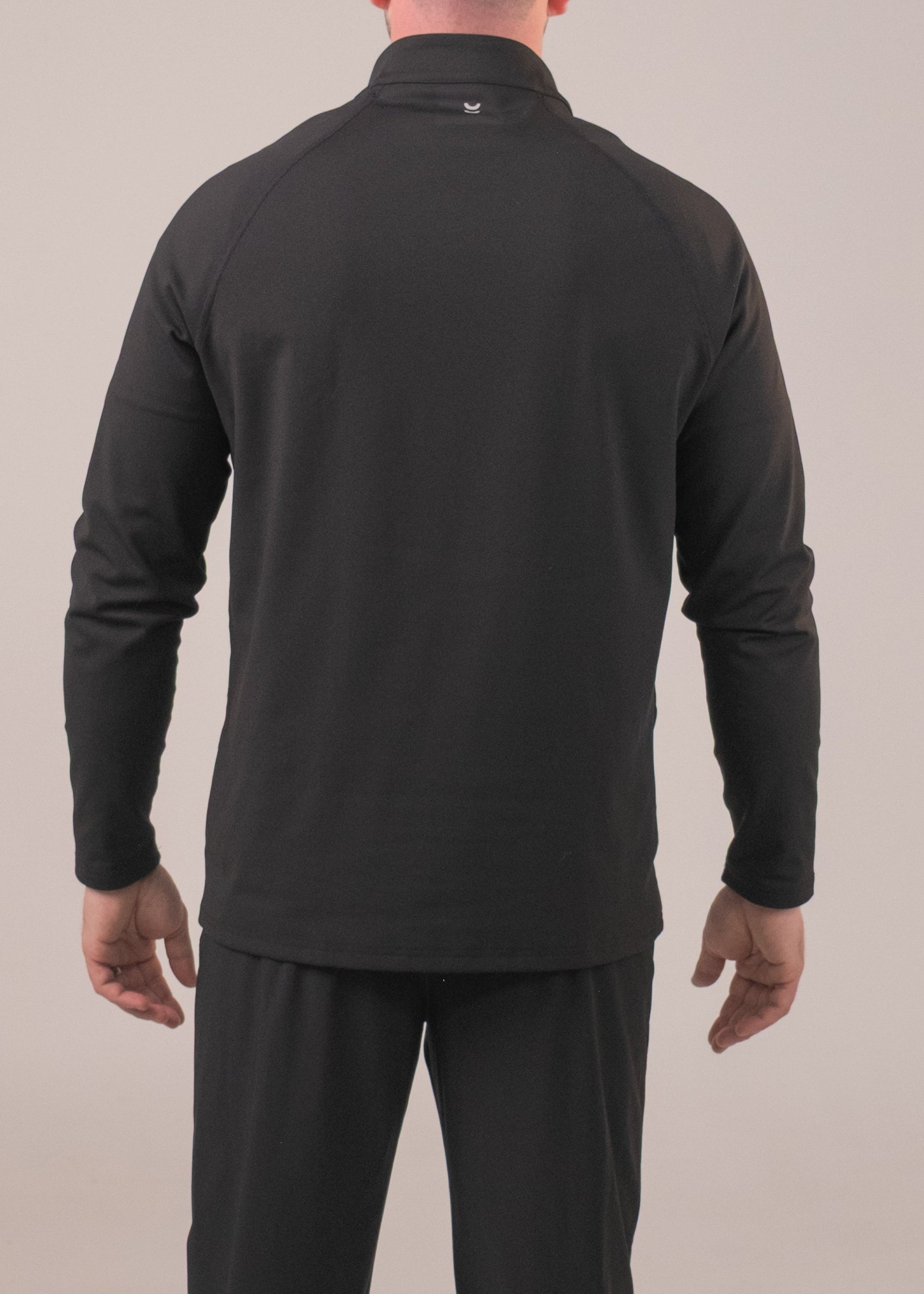Person wearing a black long-sleeve shirt and pants on a beige background
