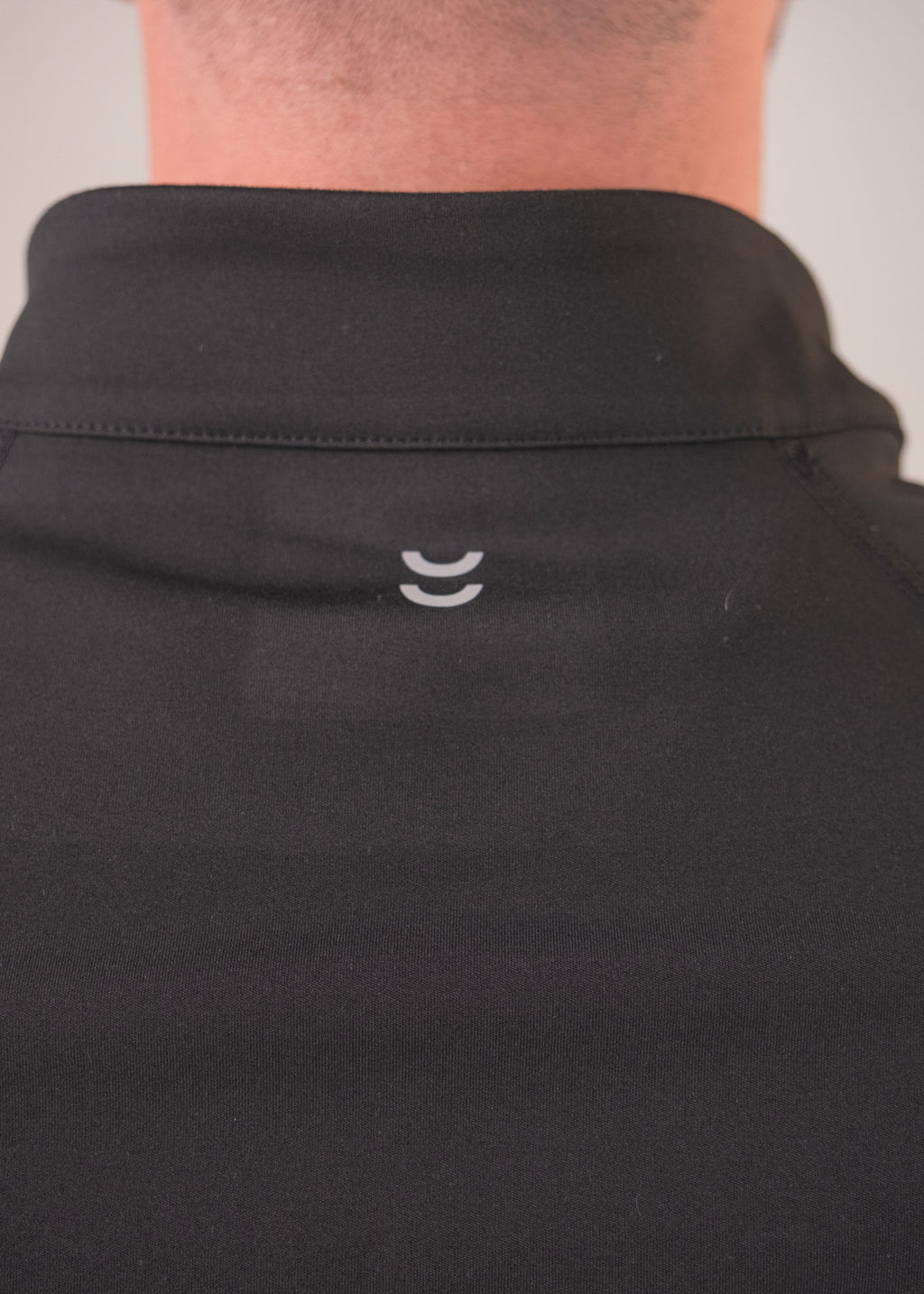 Close-up of a black shirt with a small white logo on the collar against a neutral background