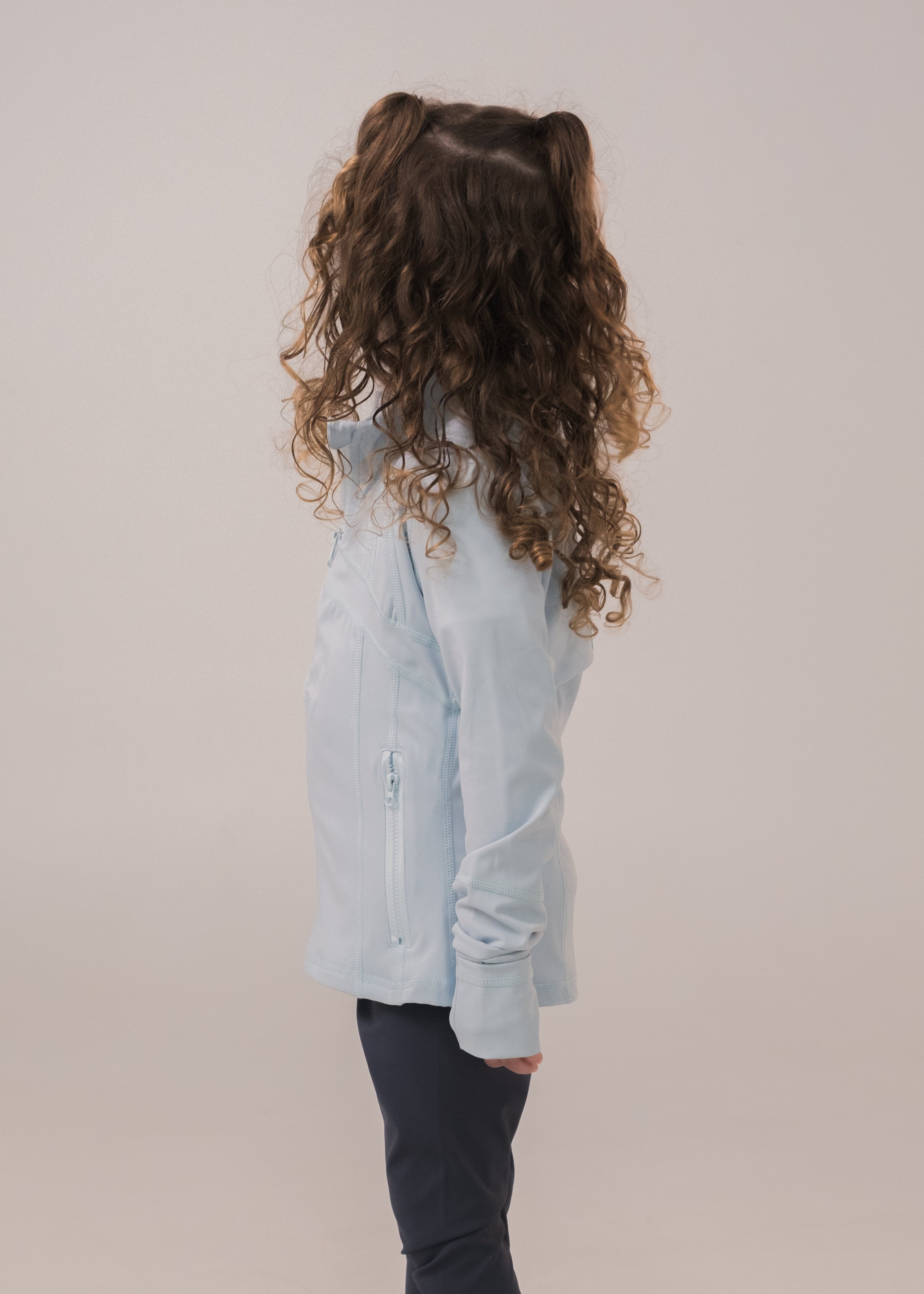 Child wearing a light blue denim shirt and dark pants on a beige background