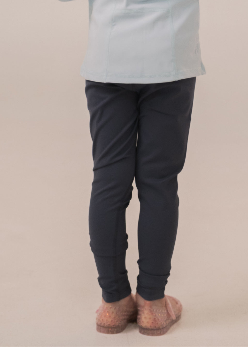 Person wearing a light blue jacket and dark pants on a beige background