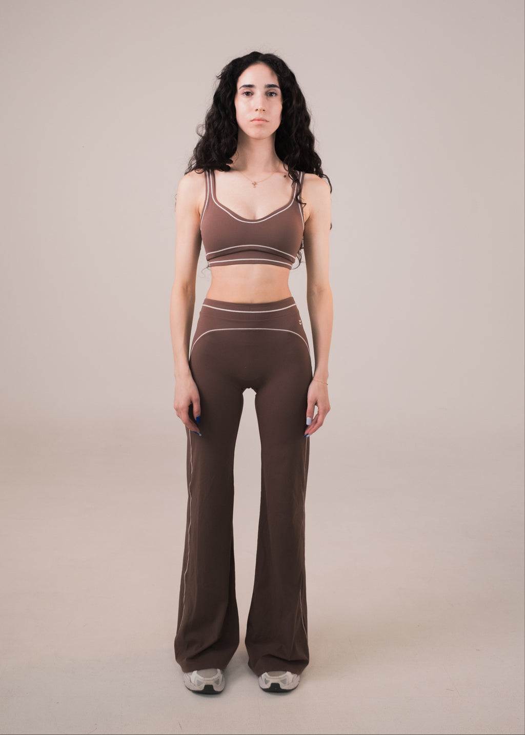 Woman wearing a brown sports bra and leggings set on a beige background