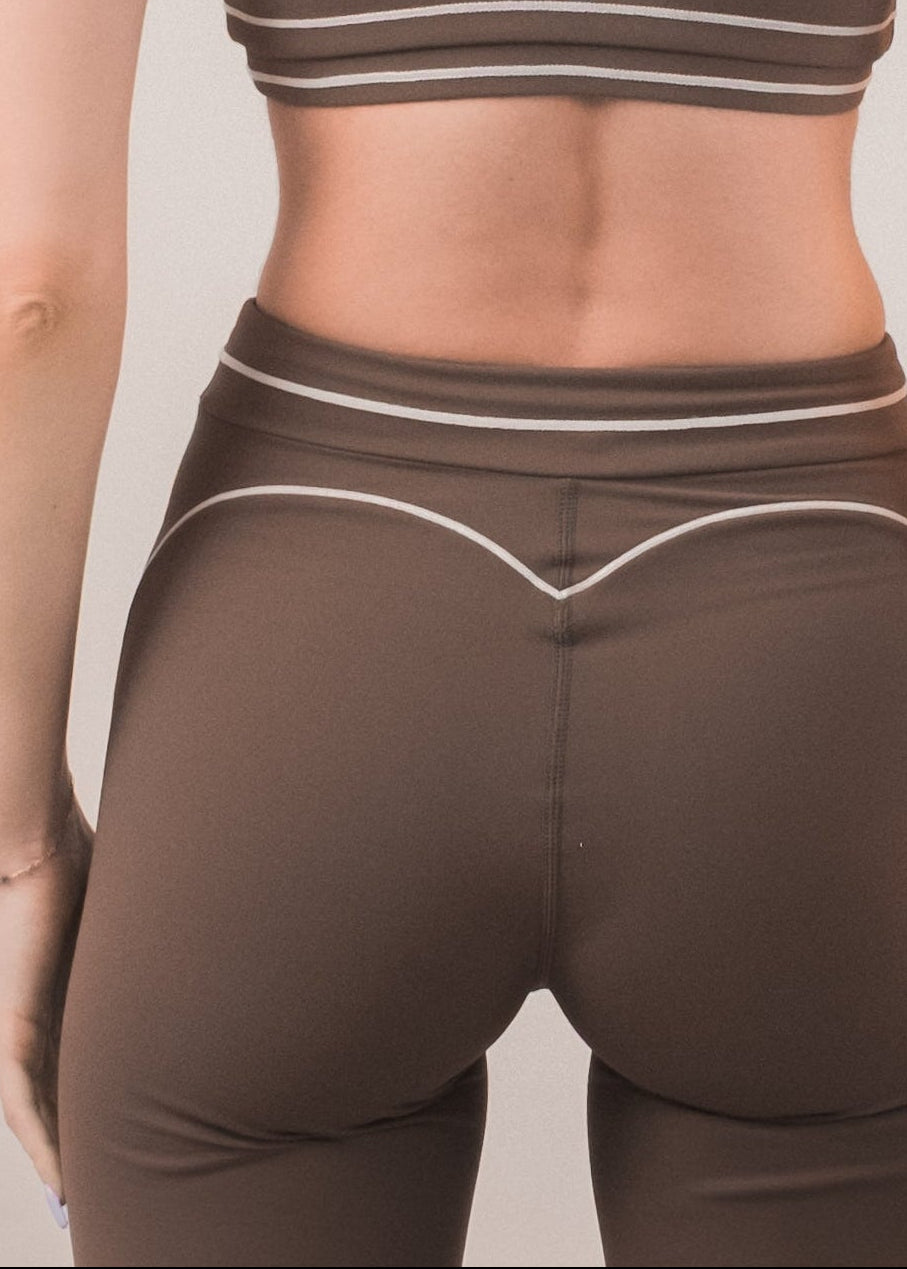 Woman wearing a brown sports bra and leggings set on a plain background
