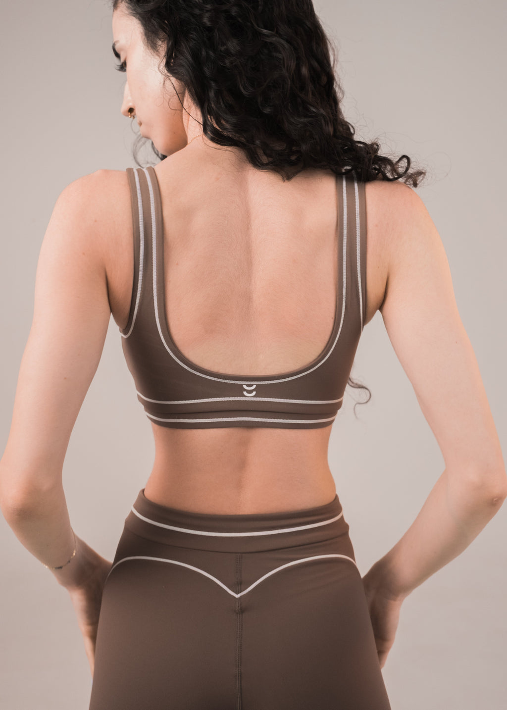 Woman wearing a brown sports bra and leggings set on a neutral background