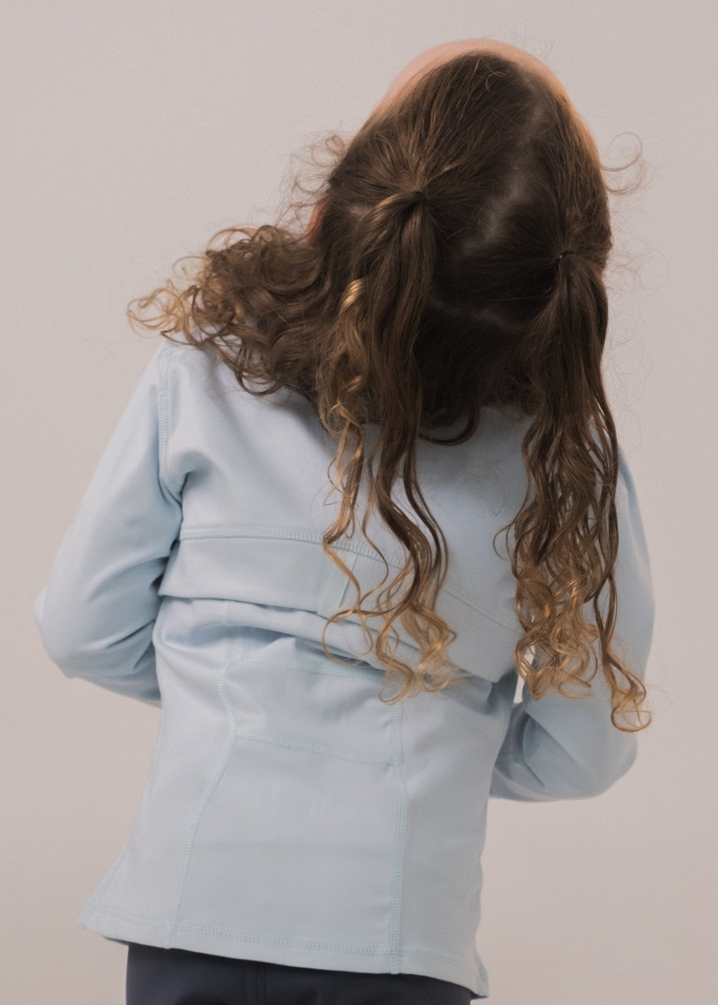 Person wearing a light blue jacket with long, wavy hair on a plain background