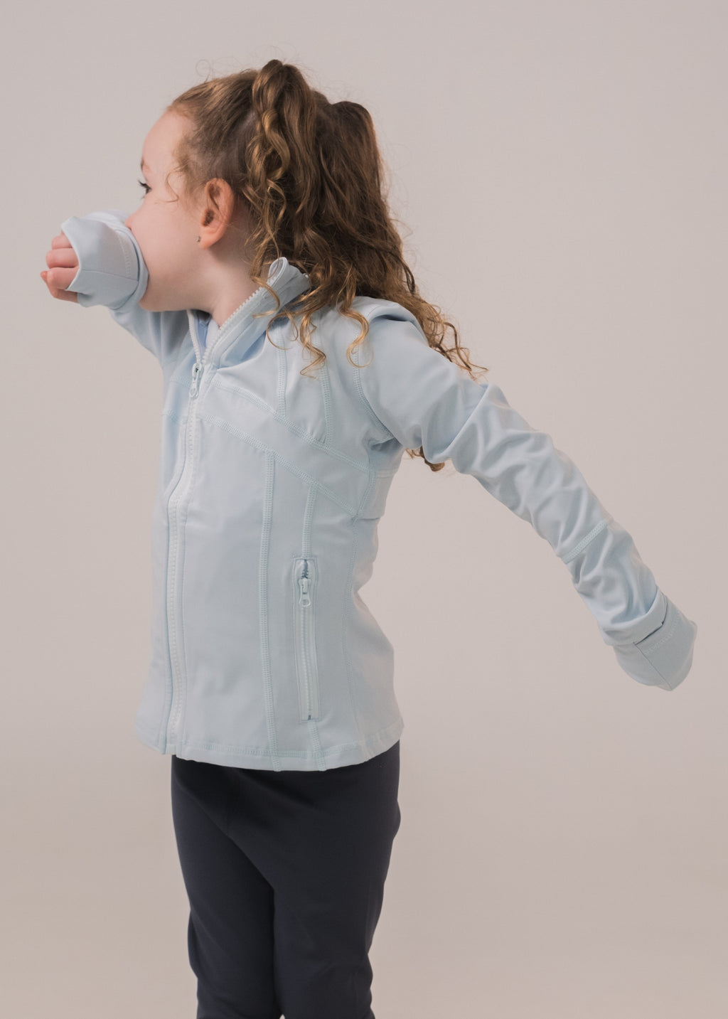 Child wearing a light blue jacket and dark pants on a plain background