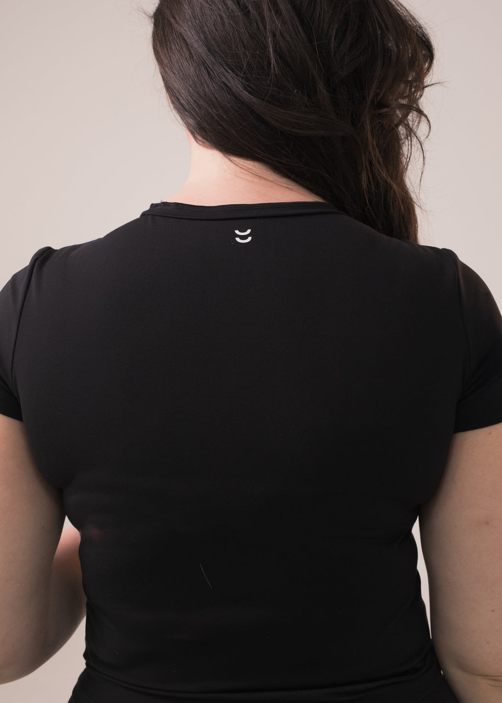 Person wearing a black top with a small logo on the back against a plain background