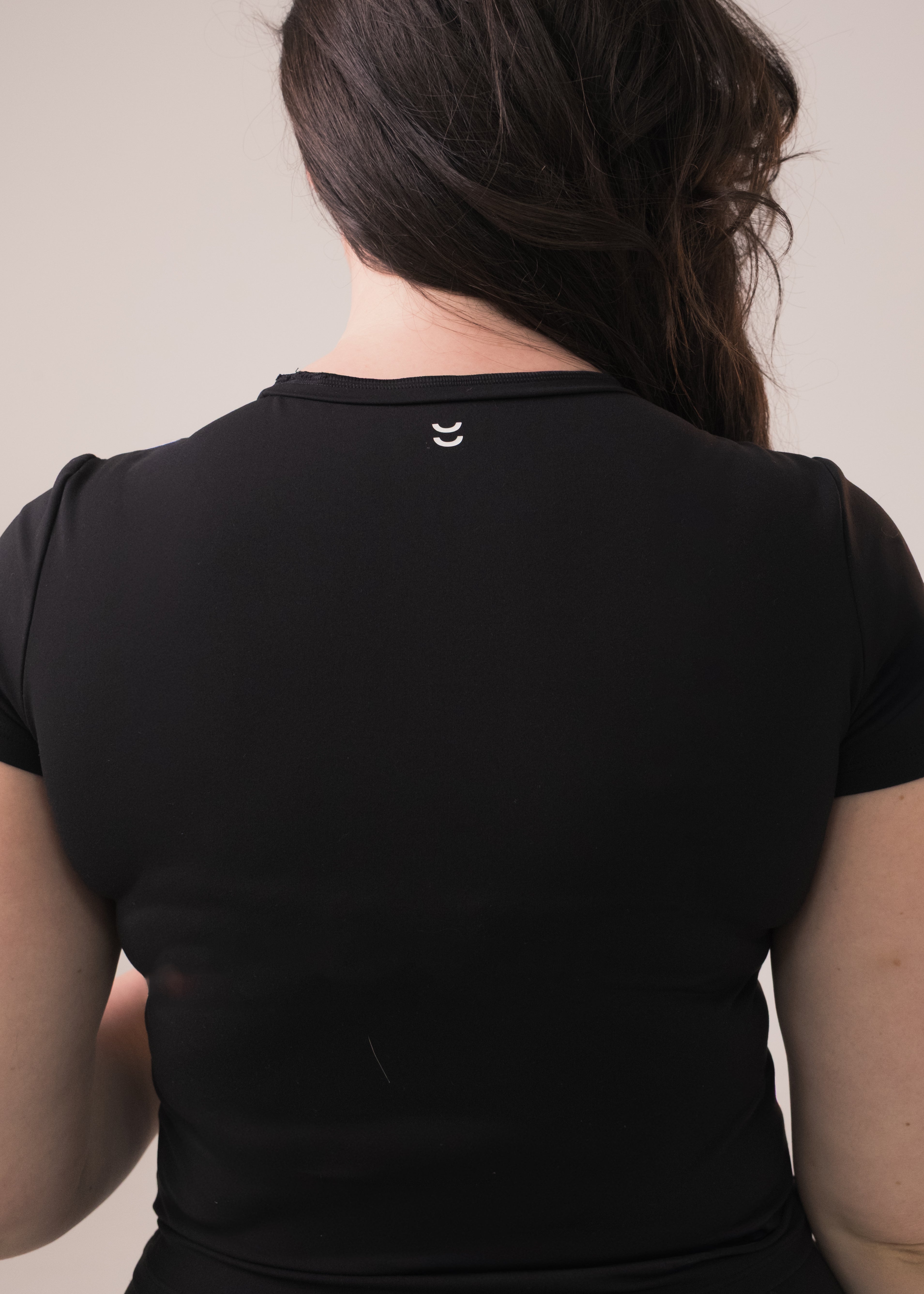 Person wearing a black top with a small logo on the back against a plain background