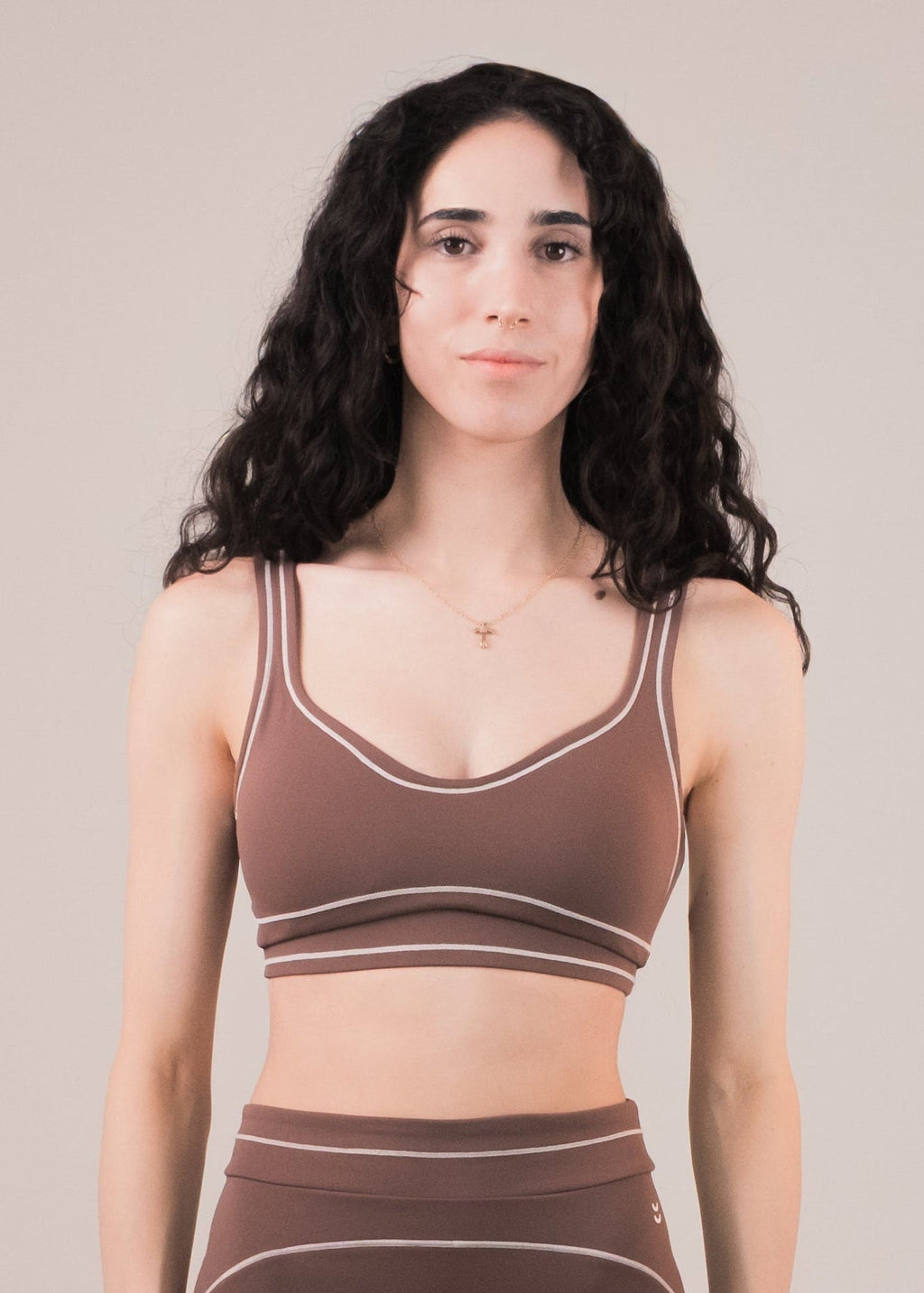 Woman wearing a brown sports bra and leggings set on a beige background