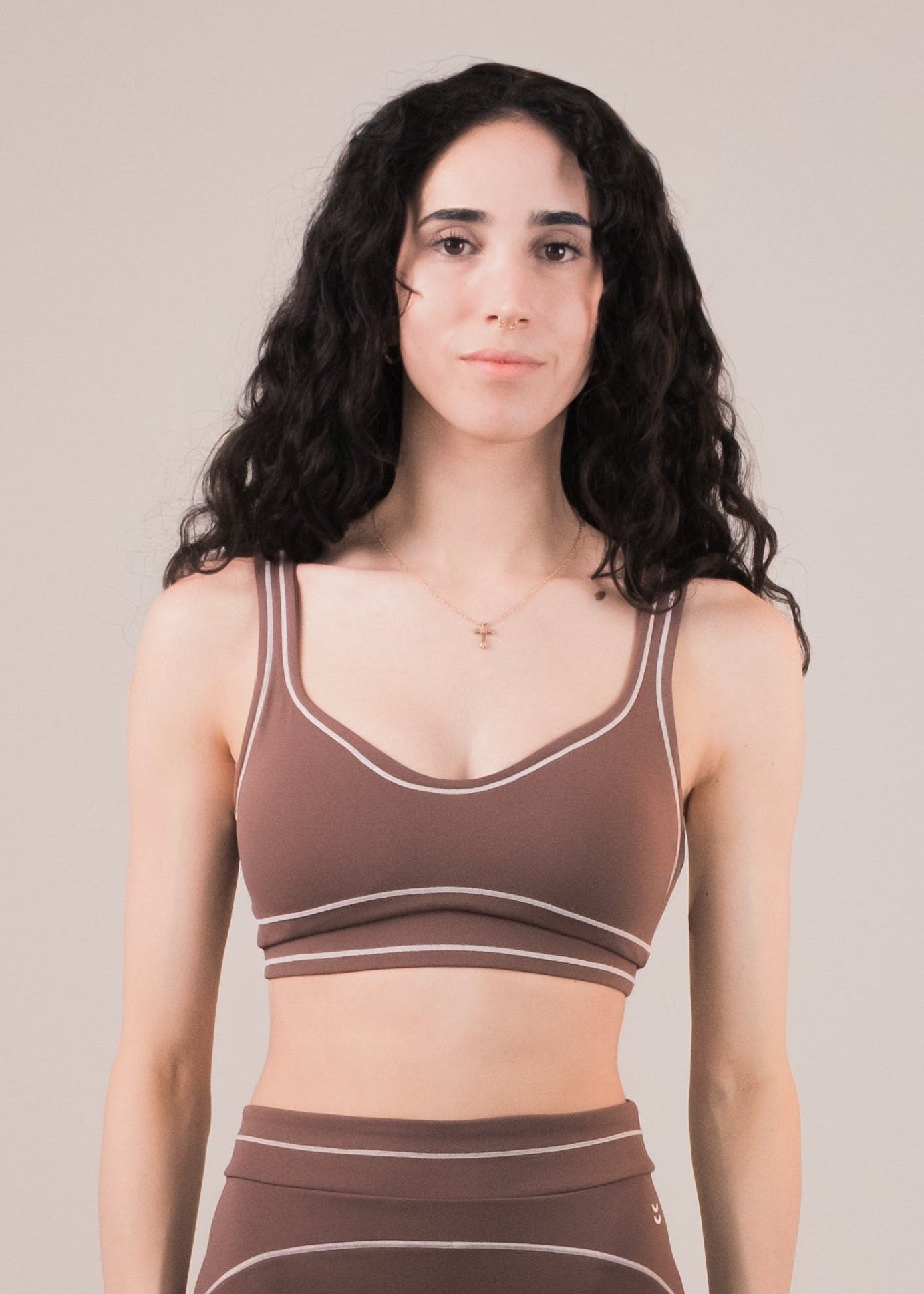 Woman wearing a brown sports bra and leggings set on a beige background