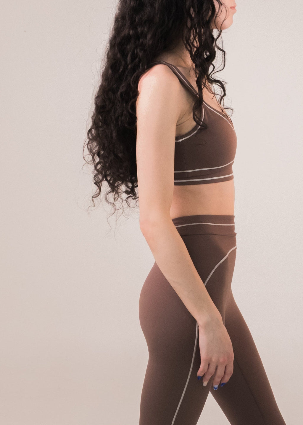 Woman wearing a brown sports bra and leggings set on a plain background
