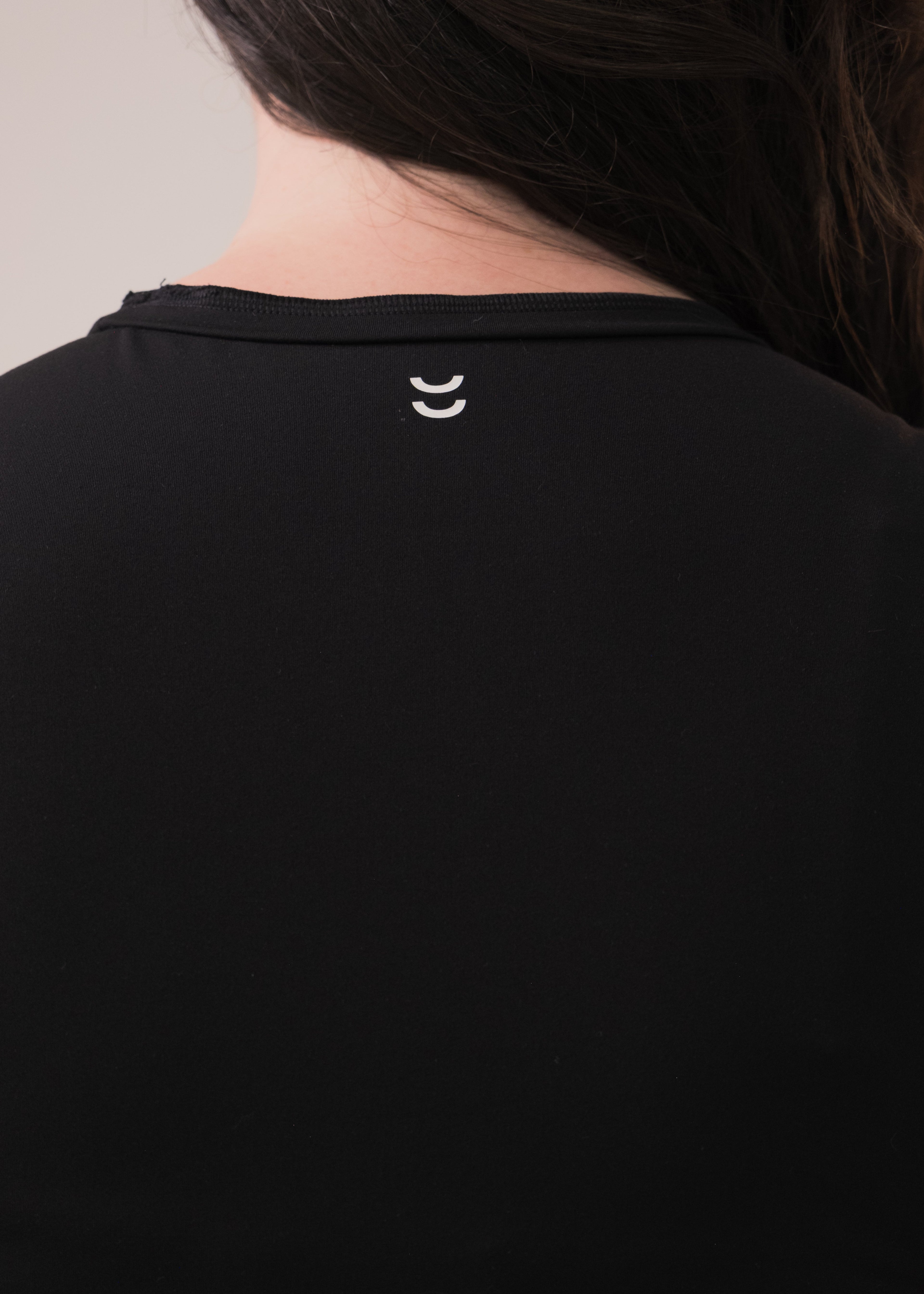 Black shirt with a small white logo on the collar against a neutral background