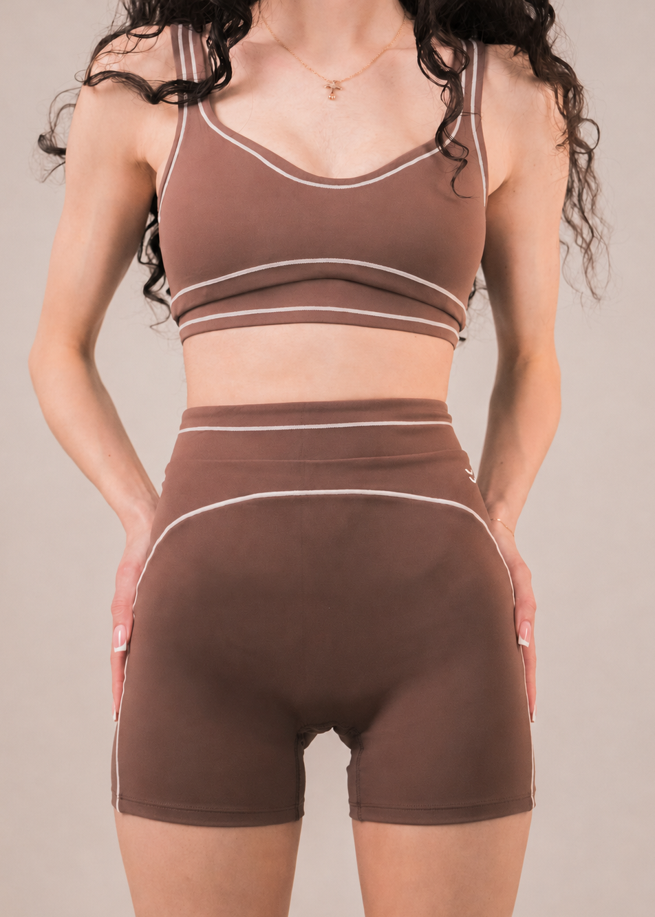 Woman wearing a brown sports bra and shorts set on a beige background