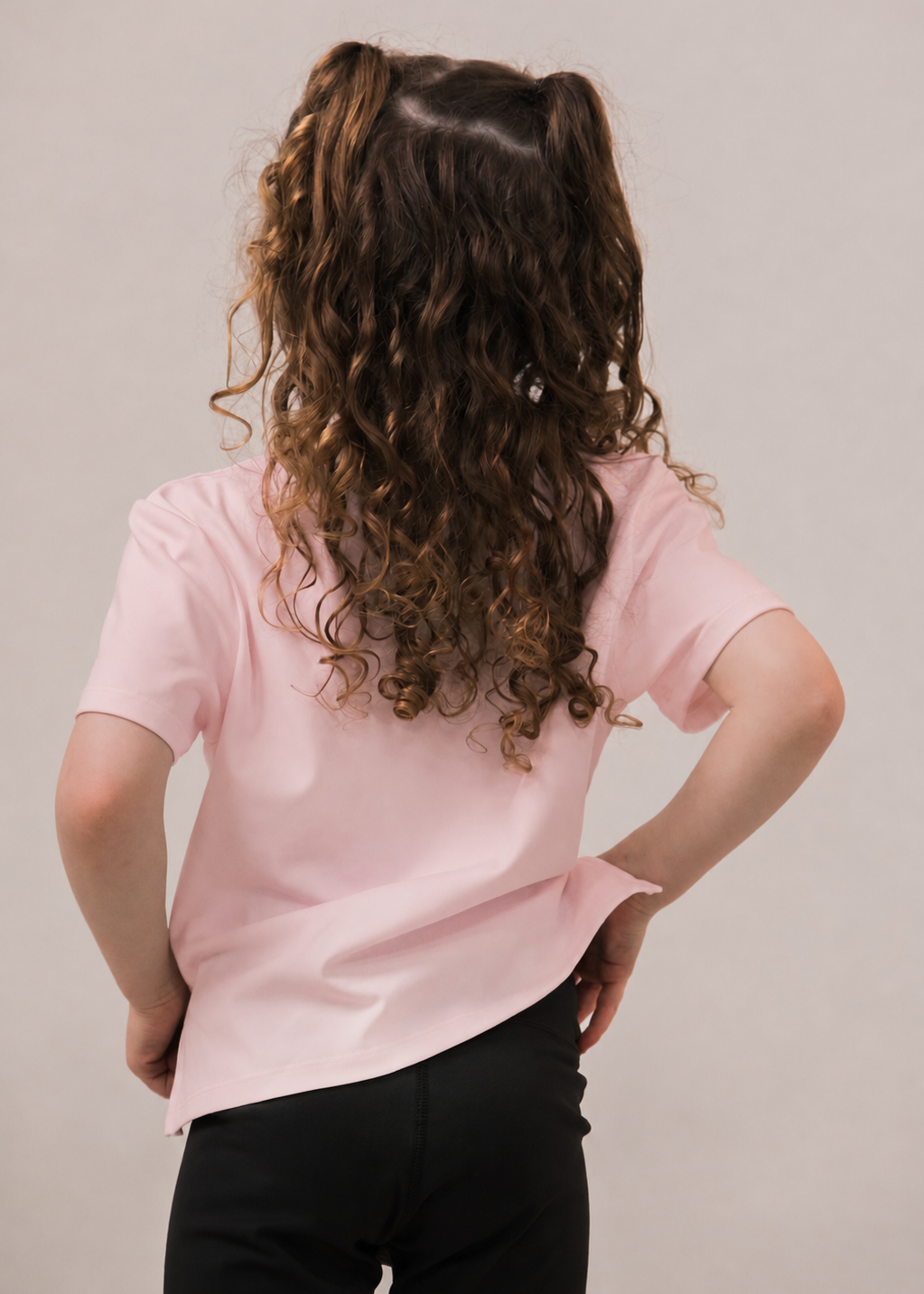 Person wearing a pink shirt and black pants with a neutral background