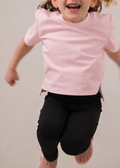 Child wearing a pink shirt and black leggings running on a plain background