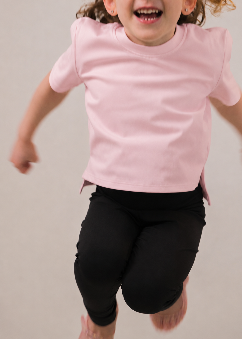 Child wearing a pink shirt and black leggings running on a plain background